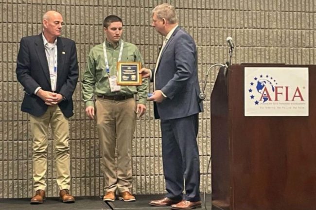 AFIA’s Gary Huddleston presents Kent Nutrition Group representatives Jason Lents, center, and Duke Tanguy, left, with the 2021 AFIA/Feedstuffs Commercial Dry Feed Facility of the Year award.