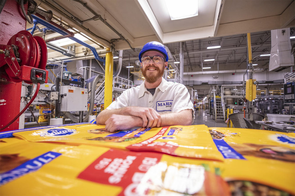 Employee smiling by PEDIGREE packaging at Mars Petcare's Mattoon, Illinois facility