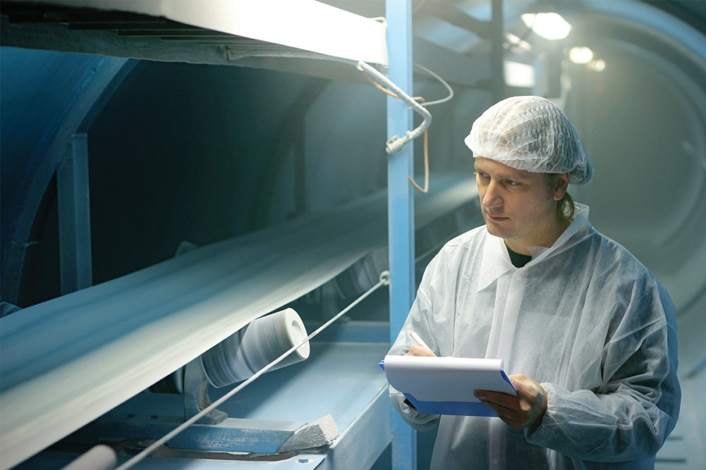 Man in white clean suit evaluating industrial processing machinery