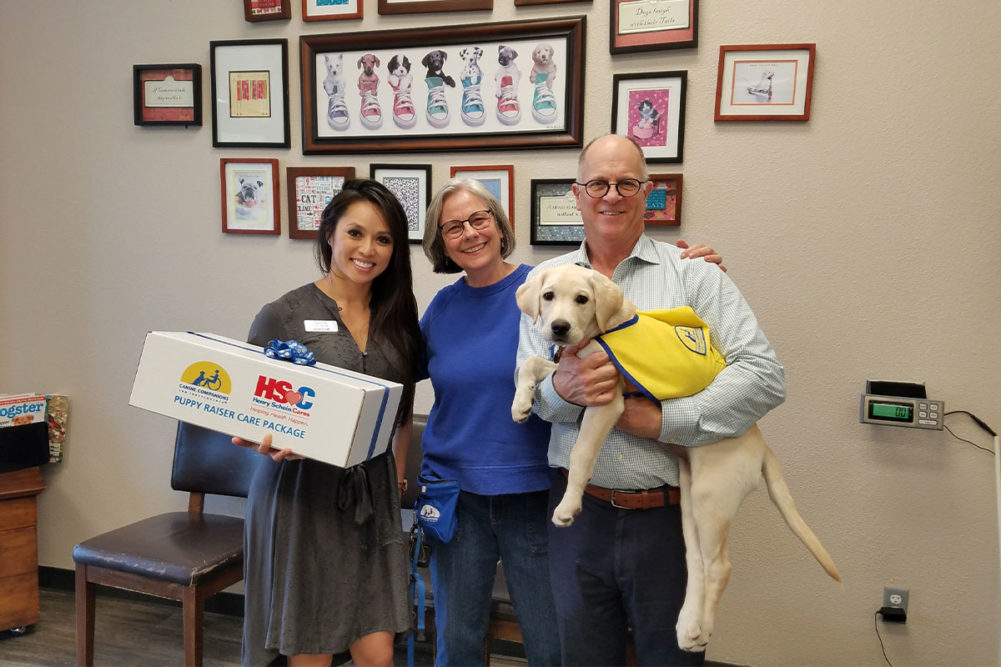 Covetrus representative Uyen Ta (left) presents 2,000th Covetrus Puppy Care Package to Canine Companions volunteer puppy raiser Kim Brewer (middle), Dr. Lee Kaplow (right) of Lakeside Pet Hospital and Fig, a future Canine Companions assistance dog.